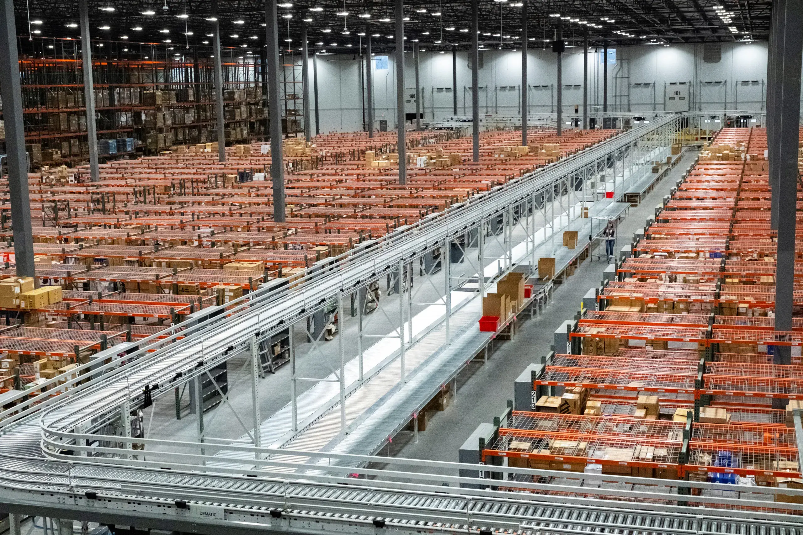 Inside a Fulfillment.com distribution center: high-bay pick modules and a powered conveyor spine running the length of the building.